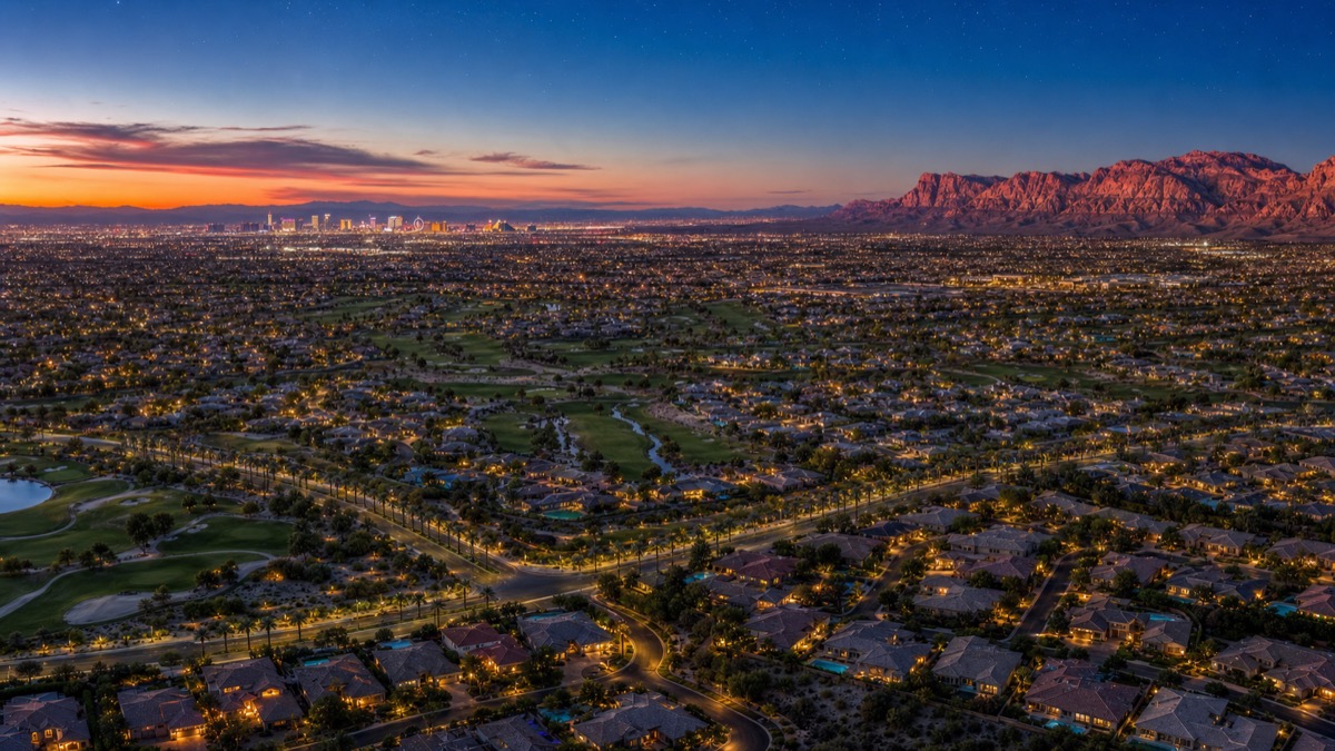 Aerial twilight overview of Summerlin showing the layered residential villages, guard-gated luxury enclaves at the western edge against Red Rock Canyon, and the Howard Hughes-designed parks and trails network connecting them